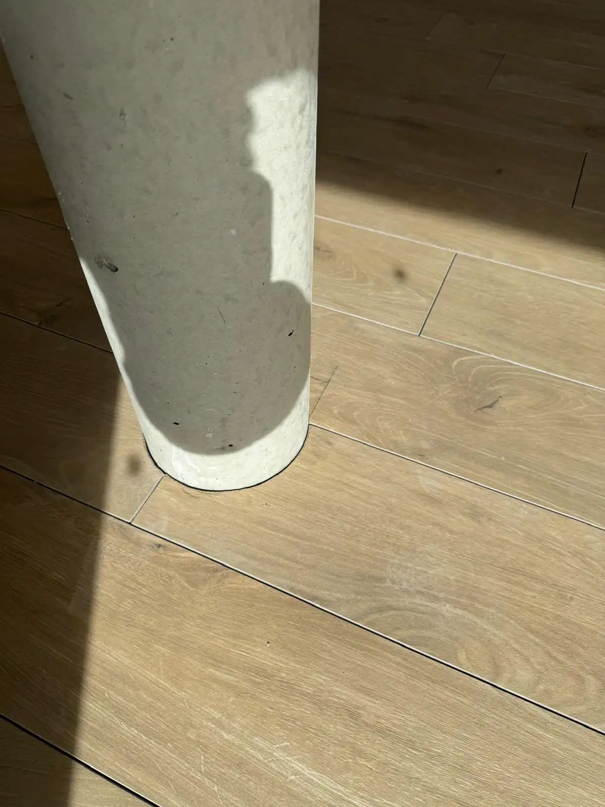 Carrelage effet bois découpé au plus près d’un poteau rond en béton, dans la lumière du soleil
