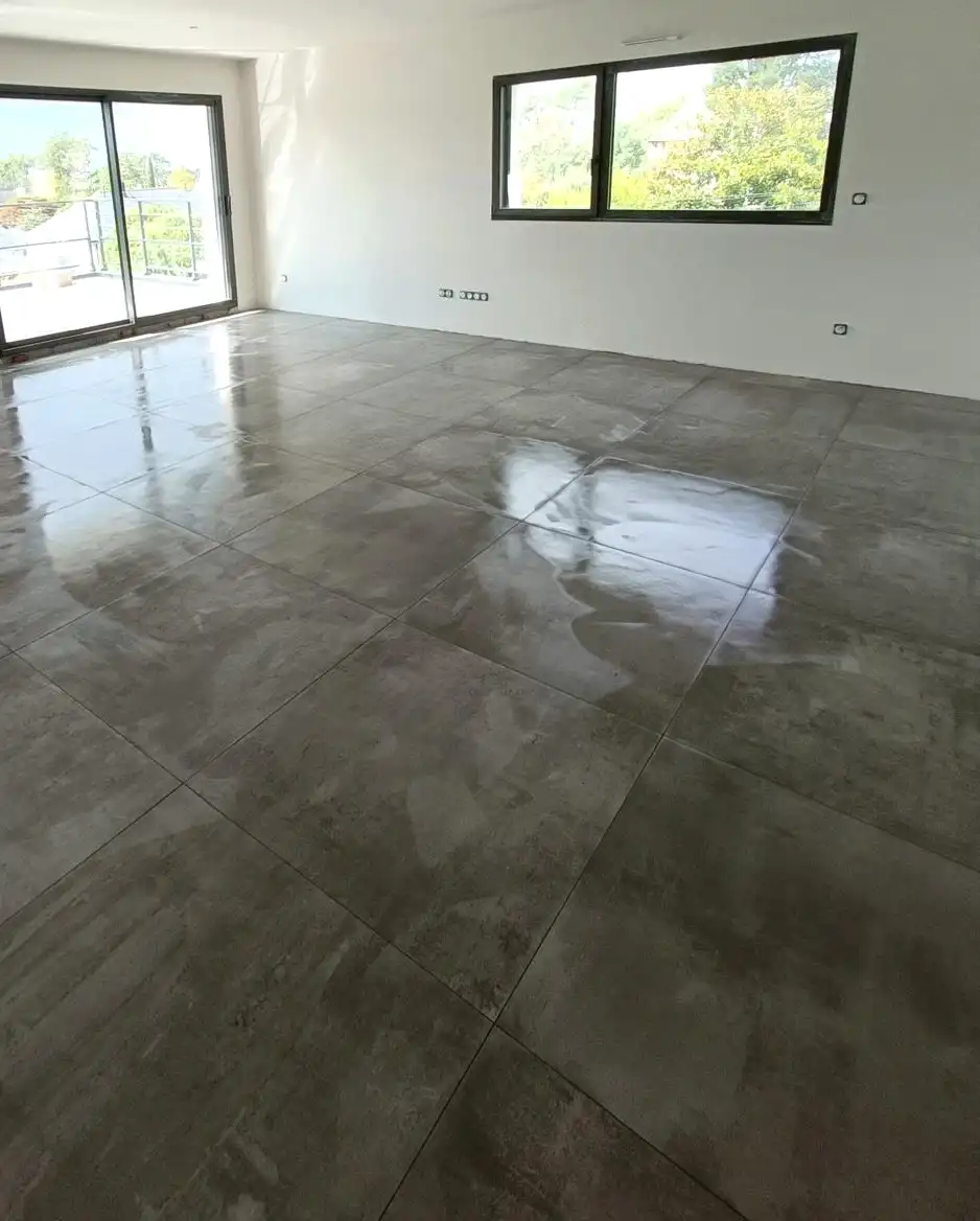 Grand séjour lumineux carrelé en grand format gris effet béton, baies vitrées ouvertes sur la terrasse