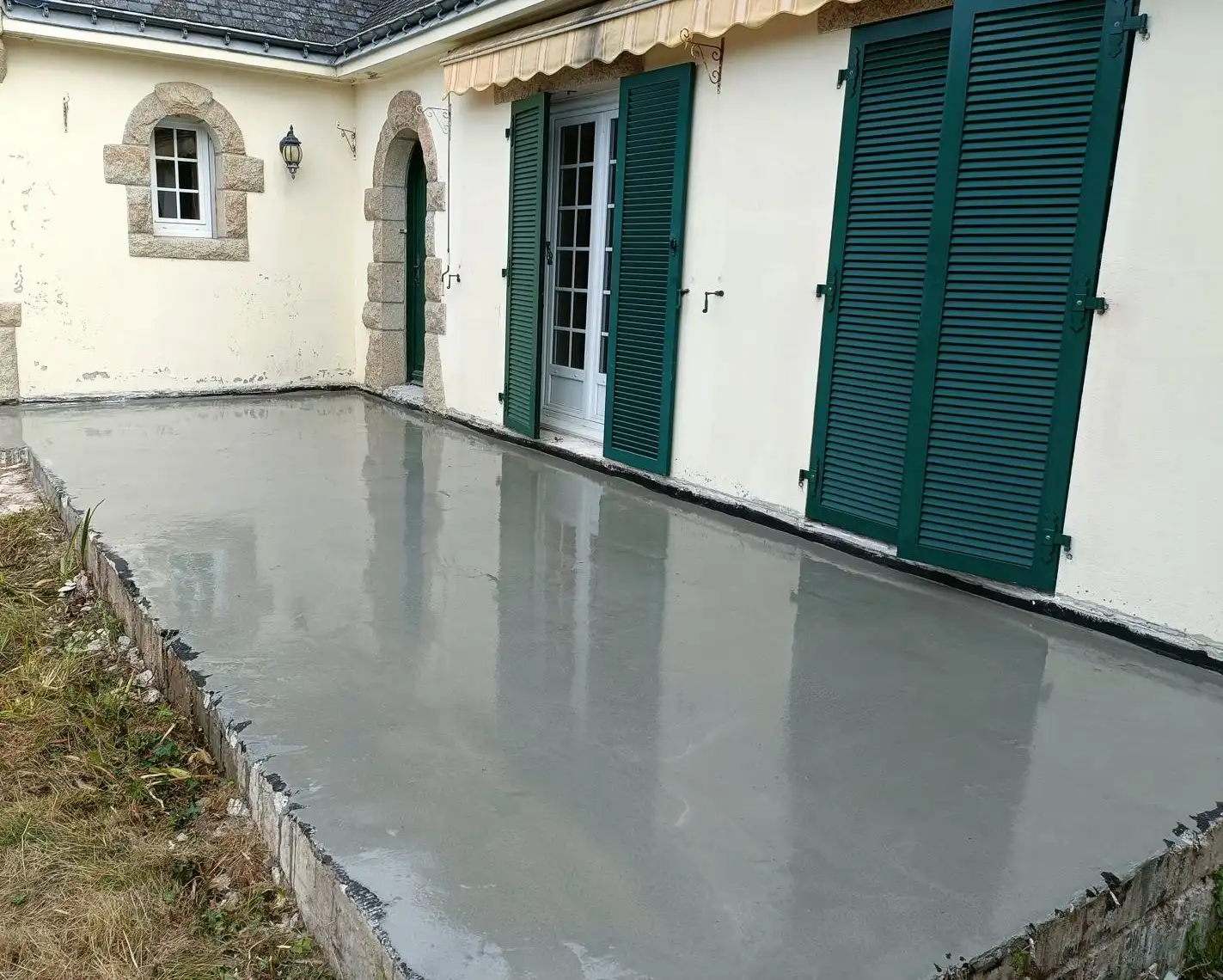 Chape extérieure fraîchement lissée sur une terrasse, le long d’une maison aux volets verts