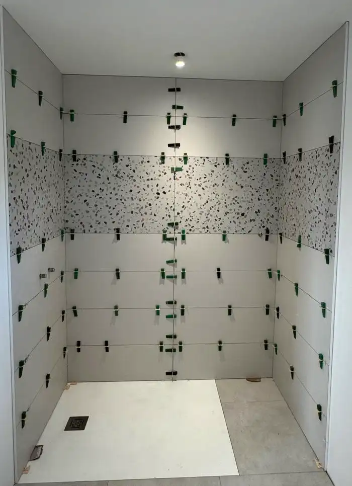 Douche de plain-pied carrelée en grands formats gris avec bandeau effet terrazzo et cales de nivellement