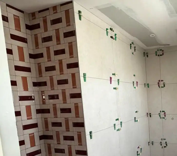 Salle de bain : mur en faïence à motif tressé bordeaux et orange, grands formats clairs avec cales de nivellement