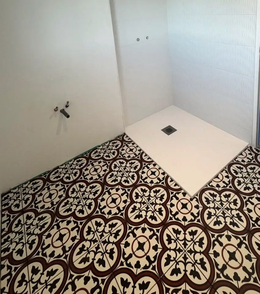 Salle de bain : sol à motifs effet carreaux de ciment rouge et noir autour d’un receveur de douche blanc