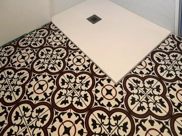 Sol de salle de bain à motifs effet carreaux de ciment rouge et noir autour d’un receveur de douche blanc