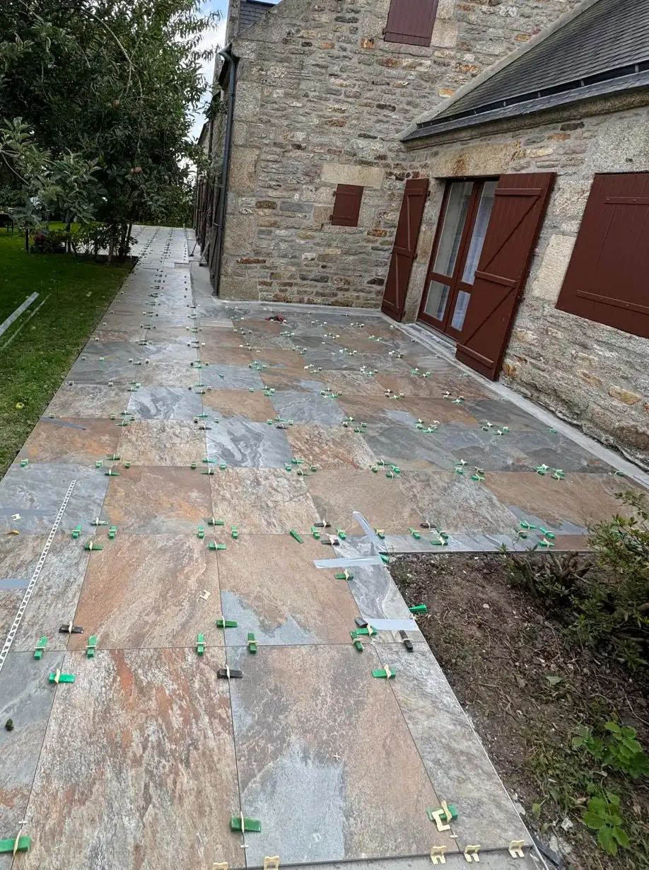 Terrasse en carrelage grand format effet ardoise le long d’une maison en pierre, avec cales de nivellement